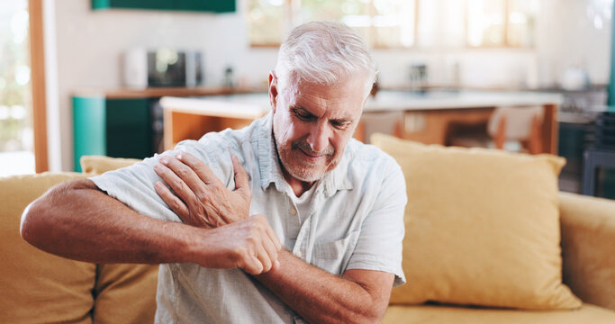 Home, shoulder pain and senior man on sofa, broken and pressure in living room. Pensioner, apartment or mature person on couch, inflammation or joint injury in lounge, stress and bruise with burnout
