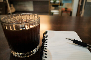A cup of Americano, placed beside a notebook and pen on a table in a cozy café, creating a relaxed and productive ambiance