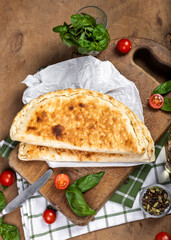 calzone with salami, ham, cheese, tomato, basil, mushrooms, cream sauce on a wooden background, Italian pastries, traditional Italian cuisine, olive oil with spices, food photo, flatlay