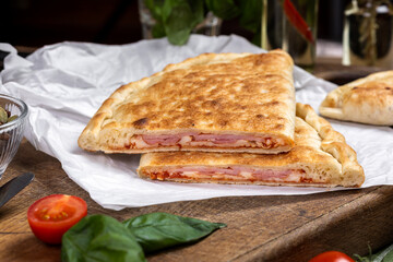 calzone with salami, ham, cheese, tomato, basil, mushrooms, cream sauce on a wooden background, Italian pastries, traditional Italian cuisine, olive oil with spices, food photo, flatlay