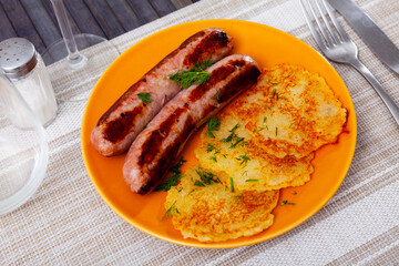 National dish of Belarusian cuisine is draniki, made from grated potatoes, served on a plate with fried sausages and ..decorated with herbs on top
