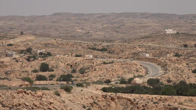 Car drives through arid mountain desert landscape in Matmata region, transportation and infrastructure in Tunisia
