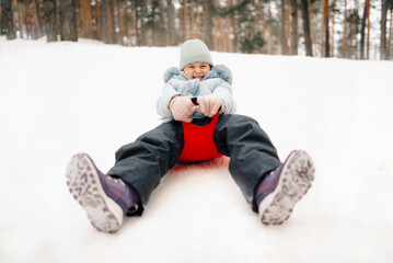 Girl sliding downhill on a red sled in snowy forest, enjoying winter fun