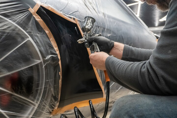 Painting technician applying a coat of paint on the fender of the car.  Local repair of car...