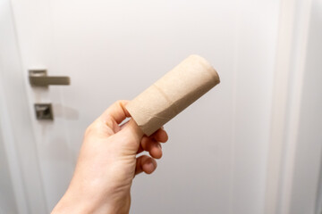 Man's hand taking an empty toilet paper in a WC. Empty toilet paper roll in hand. Man's hand holding brown paper tube close-up. 