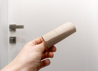 Man's hand taking an empty toilet paper in a WC. Empty toilet paper roll in hand. Man's hand holding brown paper tube close-up. 