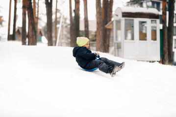 Happy child sliding down on a snowy hill in winter