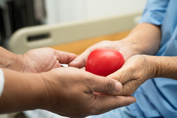 Doctor give red heart to Asian elderly woman patient in her hand on bed in hospital.