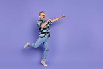Happy stylish man dancing and expressing joy in casual outfit with violet background