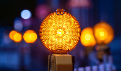 Bright yellow-orange flashing lights at a roadworks site in Germany at night. Warning lights with intense colours protect against accidents at obstacles and danger spots on the road. Selective focus.