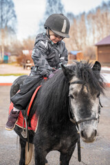 Little cute girl riding a little horse or pony in the winter in field in the winter