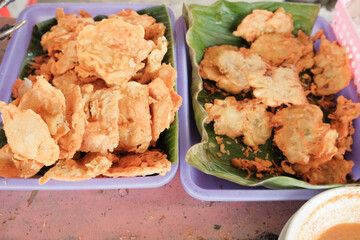 A serving of crispy battered fried tempeh (Tempe Goreng Tepung) and vegetable fritters (Bakwan) displayed at a traditional food stall. A popular Indonesian street snack