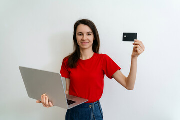 Naklejka premium Happy woman in hat holding credit card and laptop isolated over white background