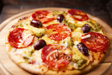 Pizza with chorizo ​​sausage, mozzarella and cheddar cheese, olive pesto and kalamata olives. Wooden background. Soft focus. Close up.