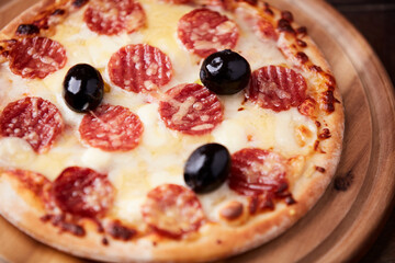 Pizza with salami, mozzarella and cheddar cheese. Wooden background. Soft focus. Close up.