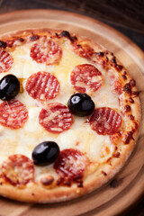 Pizza with salami, mozzarella and cheddar cheese. Wooden background. Soft focus. Close up.