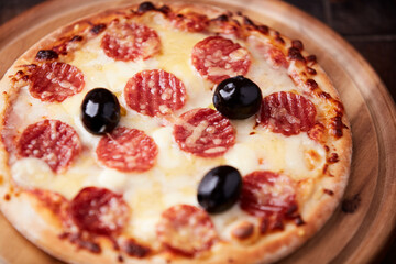 Pizza with salami, mozzarella and cheddar cheese. Wooden background. Soft focus. Close up.
