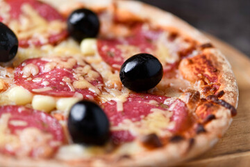 Pizza with salami, mozzarella and cheddar cheese. Wooden background. Soft focus. Close up.