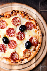 Pizza with salami, mozzarella and cheddar cheese. Wooden background. Soft focus. Close up.