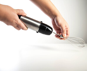 Modern immersion blender with whisk in hand on white background, close-up