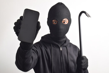 Mysterious man wearing black hoodie and mask doing hacking activity on mobile phone, hacker holding...