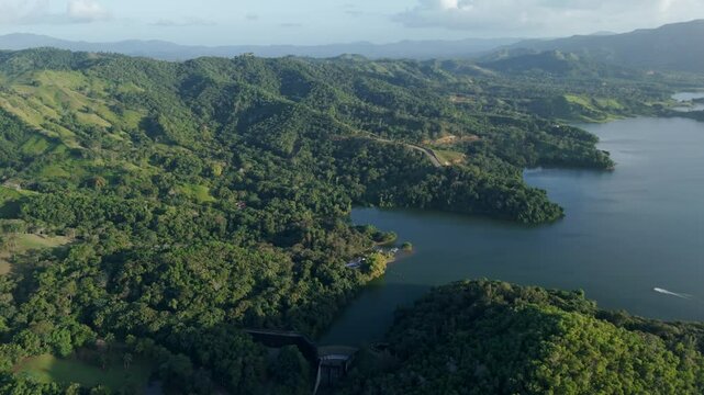 Cinematic drone shot of cruising boat on Water reserve with Dam in Dominican Republic. Green tropical mountains and Hatillo Dam on Dominican Republic island. Wide shot.