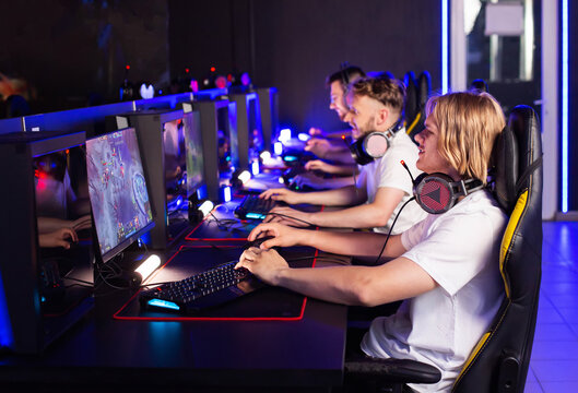 Five Caucasian gamers of different ages are playing strategy game in computer club. Multiplayer online game in modern cyber space cafe with desktop computers. Cyber team plays shooter, tournament