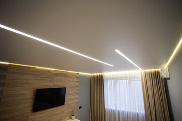 Beautiful modern stylish ceiling with light lines against the background of a window with curtains...