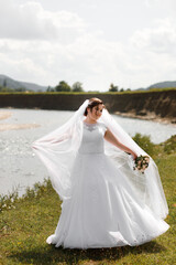 a woman in a wedding dress stands in an open field. She is wearing a white dress with lace elements and a long veil. She has dark hair tied up in an updo.