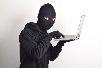 Mysterious man wearing black hoodie and mask doing computer hacking activity, stealing personal...