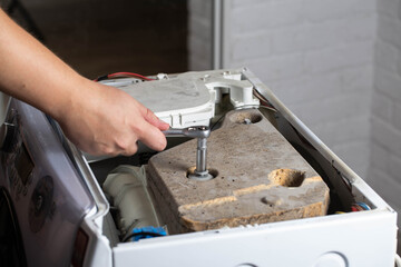 A washing machine repairman tightens the counterweight in the washing machine due to noise and vibration. Copy space for text