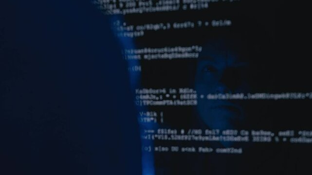 Close-up of a woman hacker's face reflected on the screen as she writes code, highlighting her intense focus.