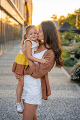 Portrait of mom and her little daughter playing on city street it sunset lights in summer