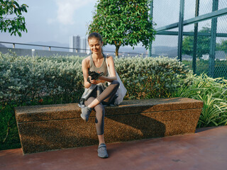Young woman sitting on a bench, smiling while using her smartphone in an outdoor park setting