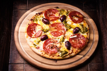 Pizza with chorizo ​​sausage, mozzarella and cheddar cheese, olive pesto and kalamata olives. Wooden background. Soft focus. Close up.