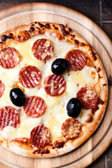 Pizza with salami, mozzarella and cheddar cheese. Wooden background. Soft focus. Close up.