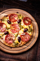 Pizza with chorizo ​​sausage, mozzarella and cheddar cheese, olive pesto and kalamata olives. Wooden background. Soft focus. Close up.