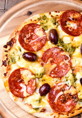 Pizza with chorizo ​​sausage, mozzarella and cheddar cheese, olive pesto and kalamata olives. Wooden background. Soft focus. Close up.