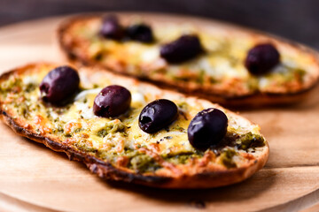Bruschetta with mozzarella and cheddar cheese, olive pesto and kalamata olives on wooden background. Soft focus. Close up
