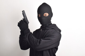 Mysterious man wearing black hoodie and mask holding gun, isolated on white background.