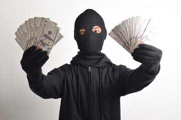 Thief wearing black jacket and mask showing dollar bills isolated on white background. Robbery and...