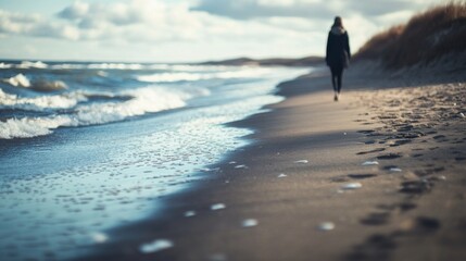 A solitary figure walks along a serene beach, with gentle waves lapping at the shore under cloudy skies