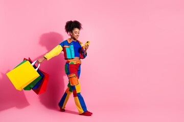 Stylish young woman with colorful shopping bags on a pink background, smiling joyfully and viewing...