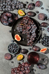 Top view of fresh dark grapes, figs, blueberries, and plums arranged on a rustic stone background.