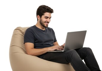 Smiling young man sitting on a beige bean bag while working on a laptop isolated on white background