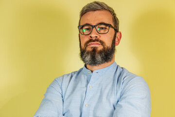 A man with a beard and glasses stands against a bright yellow backdrop