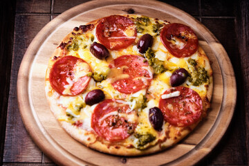 Pizza with chorizo ​​sausage, mozzarella and cheddar cheese, olive pesto and kalamata olives. Wooden background. Soft focus. Close up.	