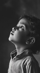 In a serene black-and-white portrait, a young Indian child gazes upward, embodying innocence and wonder. The soft contours of their face highlight a moment filled with dreams and curiosity