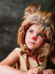 Child wearing a furry animal hat with a red nose engages in playful imagination indoors