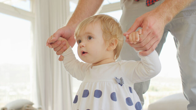 Close Up Of Father Helping Baby Daughter To Take First Steps At Home - Powered by Adobe